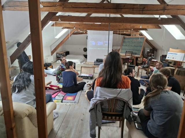 Participants seated on the floor and chairs watching a projection in the attic studio, seen through a wooden frame