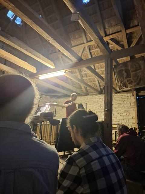 Performer at a cymbal in a stone barn, audience in the foreground