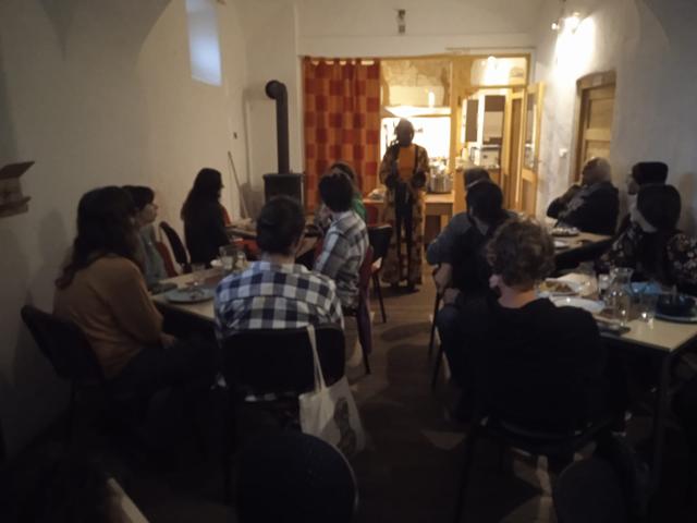 Evening event in a vaulted room, speaker standing by the kitchen door
