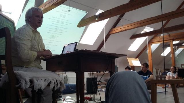 Speaker at a table in front of a projected presentation
